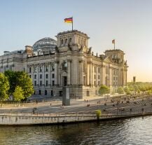 Elegancki gmach Reichstagu w Berlinie z charakterystyczną szklaną kopułą, położony nad brzegiem rzeki Spree.