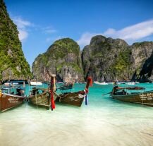 Tradycyjne łodzie na tle skał w Koh Phi Phi – jak zaplanować wakacje marzeń w Tajlandii?