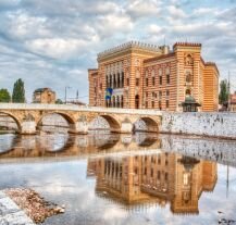 Ratusz w Sarajewie odbijający się w rzece Miljacka – stolica Bośni tworzy klimat idealny na city break w Europie.