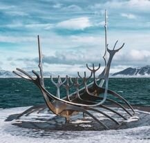 Rzeźba Sólfar (Sun Voyager) w Rejkiawiku zimą – stalowa sylwetka łodzi wikingów na tle oceanu i gór pokrytych śniegiem.